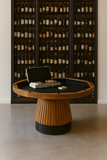 Wooden table with card games and a black suitcase in front of a wine rack.
