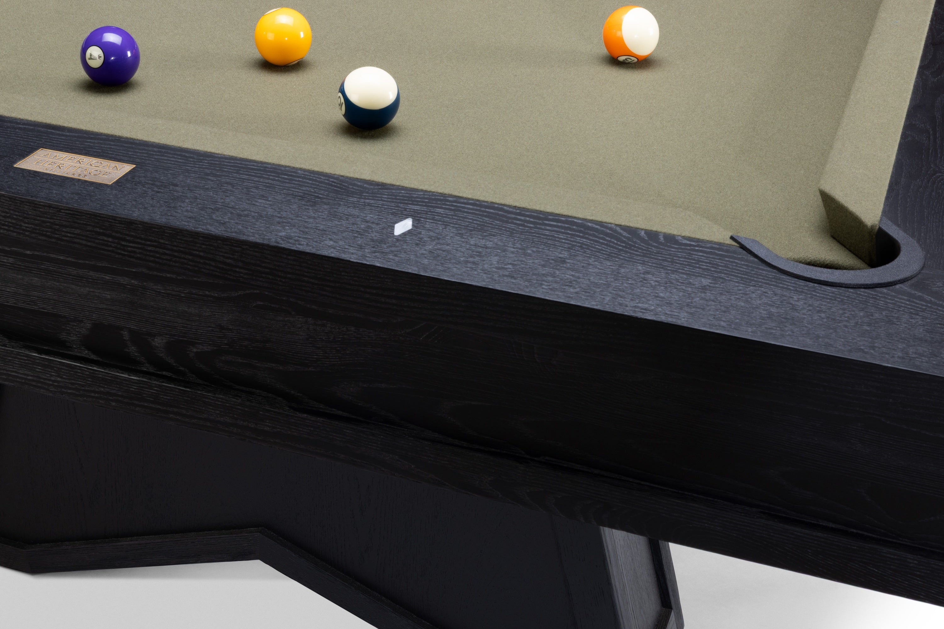 Close-up of a pool table corner with a dark wood frame, green felt surface, and several billiard balls including a purple 9-ball, yellow 8-ball, blue 7-ball, and orange/white 6-ball.