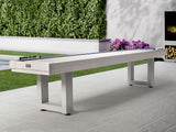 American Heritage Lanai 12' Outdoor Shuffleboard Table in Pearl White on patio with greenery.