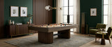 A dark wood pool table with colorful billiard balls on a gray patterned rug in a modern, stylishly decorated room with dark green walls, wooden paneling, and green armchairs.