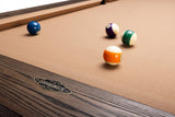 Close-up of a BenNSWIK pool table with a tan felt surface and dark wood frame, showing several billiard balls on the table.