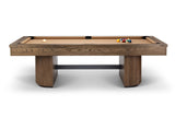 A modern pool table with a medium brown wood grain frame and legs, featuring a tan felt playing surface, a white cue ball, and a rack of colorful billiard balls, shown against a plain white background.