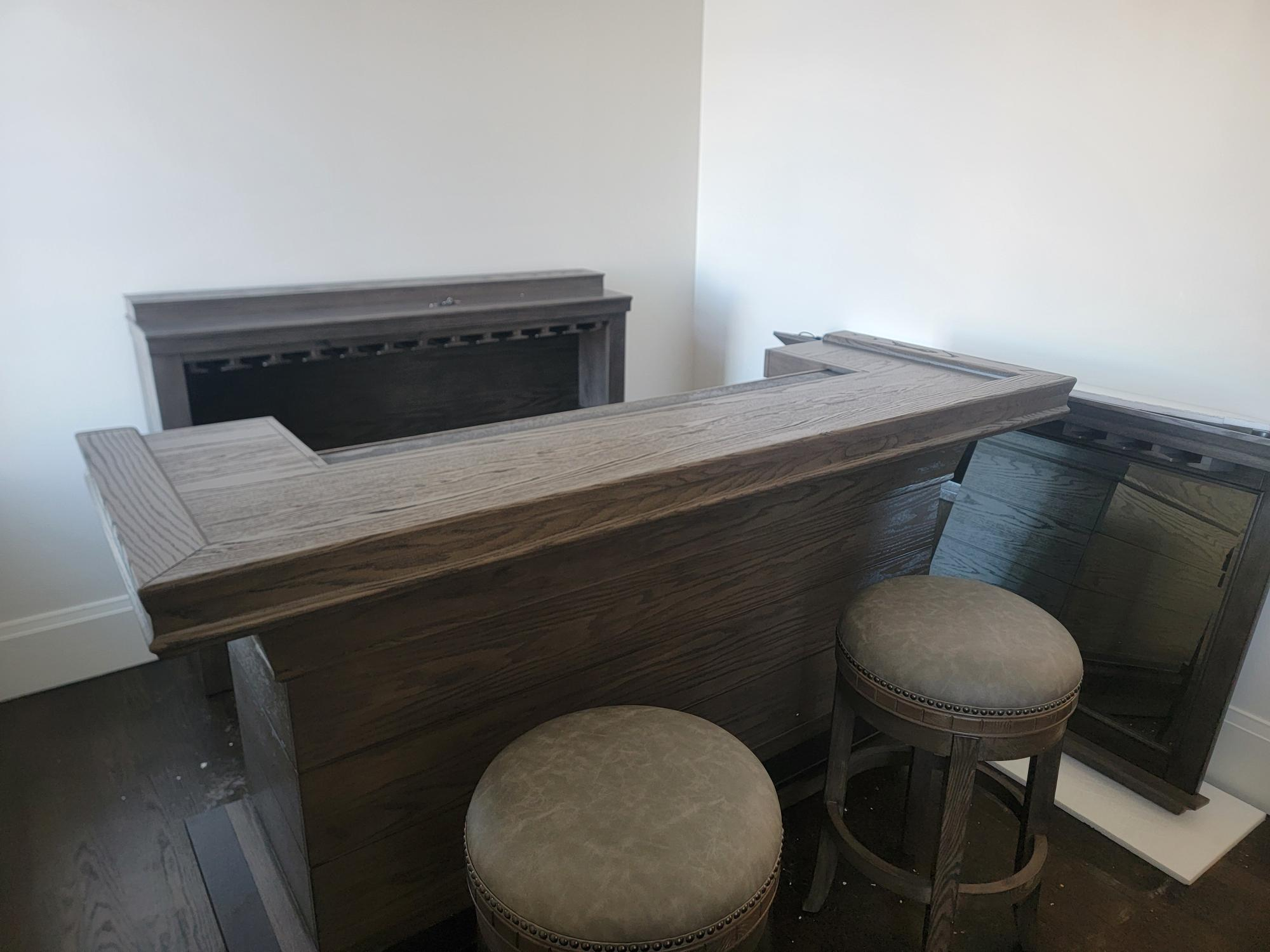 Wooden bar with two stools in a room with white walls and a fireplace.